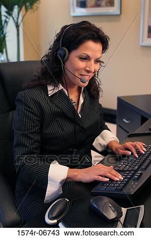 Stock Image - Side profile of a businesswoman wearing a headset working on a computer. Fotosearch