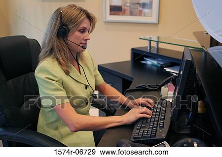 Stock Photo - Side profile of a businesswoman wearing a headset working on a computer. Fotosearch
