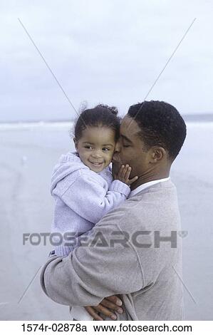 Stock Image - Side profile of a father kissing his daughter on the beach. Fotosearch
