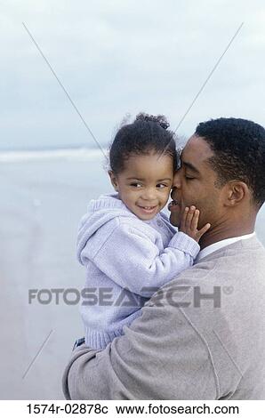 Stock Image - Side profile of a father kissing his daughter on the beach. Fotosearch