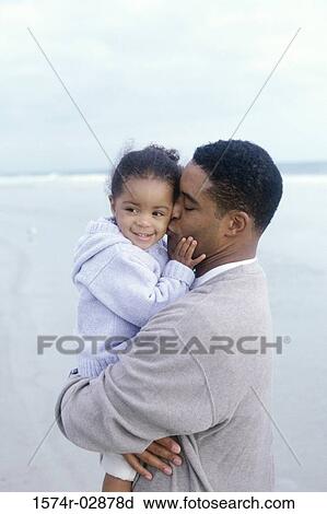 Stock Image - Side profile of a father kissing his daughter on the beach. Fotosearch