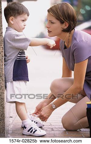 Stock Image - Side profile of a mother tying her son's shoelaces. Fotosearch