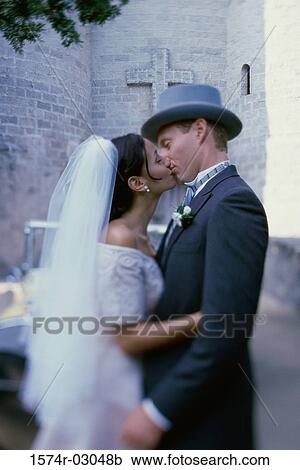 Stock Image - Side profile of a newlywed couple kissing each other. Fotosearch