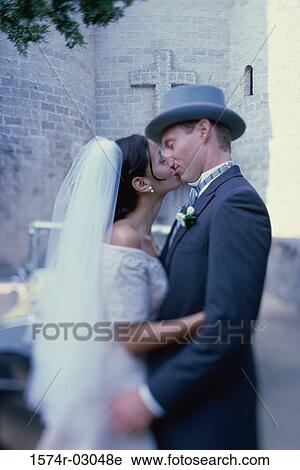 Stock Image - Side profile of a newlywed couple kissing each other. Fotosearch