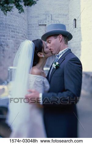 Stock Image - Side profile of a newlywed couple kissing each other. Fotosearch