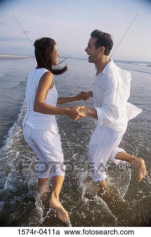 Stock Image - Side profile of a young couple playing on the beach. Fotosearch