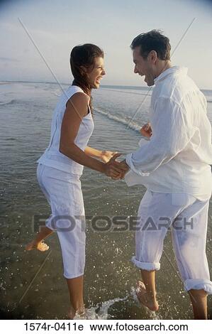 Stock Image - Side profile of a young couple playing on the beach. Fotosearch