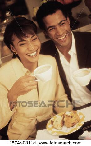 Stock Image - Smiling young couple holding cups of coffee. Fotosearch