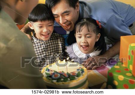 Stock Image - Son and daughter in front of a birthday cake with their parents. Fotosearch