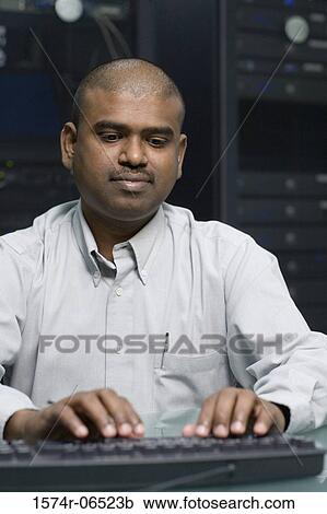Stock Image - Technician using a computer in a server room. Fotosearch