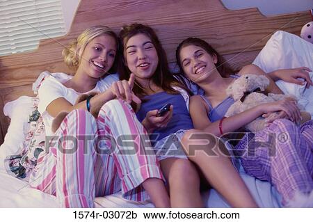 Stock Image - Three teenage girls lying on a bed watching television. Fotosearch