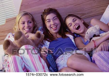 Stock Image - Three teenage girls lying on a bed watching television. Fotosearch