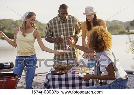 Stock Image - Three young women and a young man at an outdoor picnic together. Fotosearch