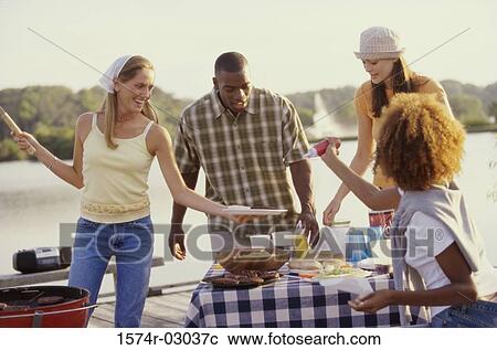 Stock Image - Three young women and a young man at an outdoor picnic together. Fotosearch