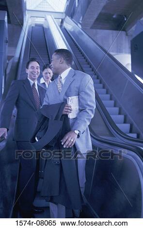 Two businessmen and a businesswoman on an escalator View Large Photo Image Stock Photography - Two businessmen and a businesswoman on an escalator. Fotosearch
