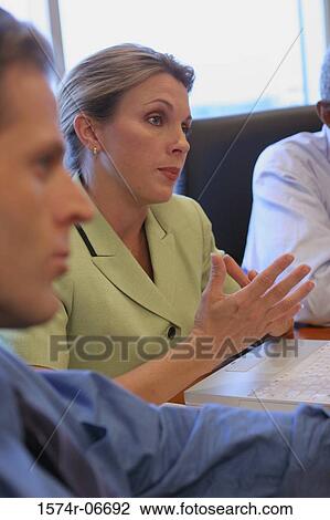 Stock Image - Two businessmen and a businesswoman sitting in a conference room. Fotosearch
