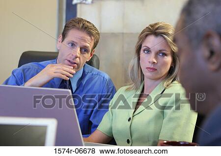 Stock Photo - Two businessmen and a businesswoman sitting in a conference room. Fotosearch
