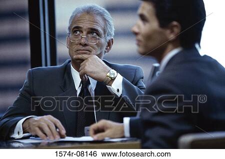 Two businessmen seated at a desk in an office View Large Photo Image Stock Photograph - Two businessmen seated at a desk in an office. Fotosearch