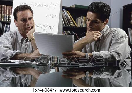 Stock Photo - Two businessmen seated at a table reading documents. Fotosearch