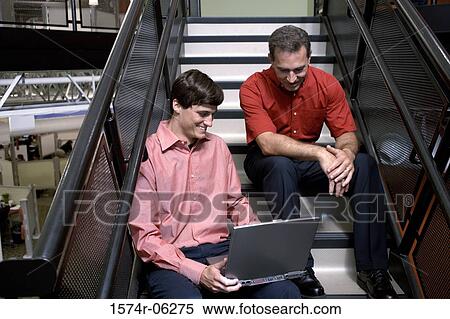 Two businessmen sitting on stairs working on a laptop View Large Photo Image Stock Photography - Two businessmen sitting on stairs working on a laptop. Fotosearch