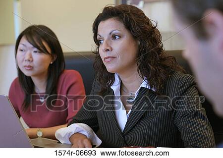 Stock Image - Two businesswomen and a businessman sitting in a conference room. Fotosearch