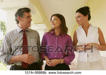 Stock Image - Two businesswomen and a businessman walking in corridor. Fotosearch