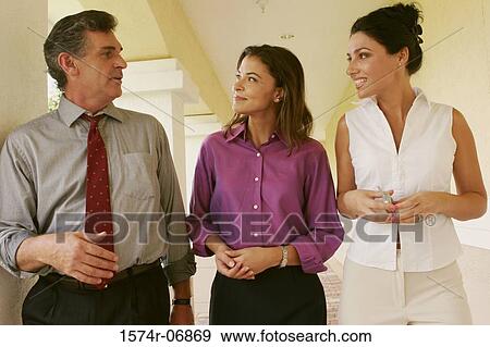 Stock Photo - Two businesswomen and a businessman walking in corridor. Fotosearch