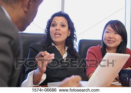 Stock Photograph - Two businesswomen and a businessman sitting in a conference room. Fotosearch