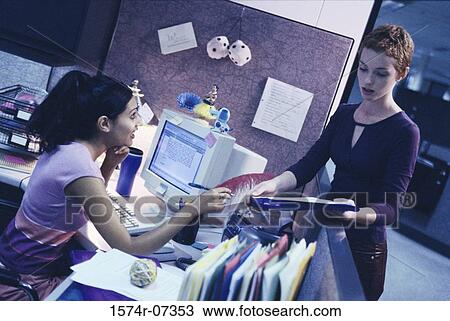 Stock Image - Two businesswomen in an office discussing documents. Fotosearch