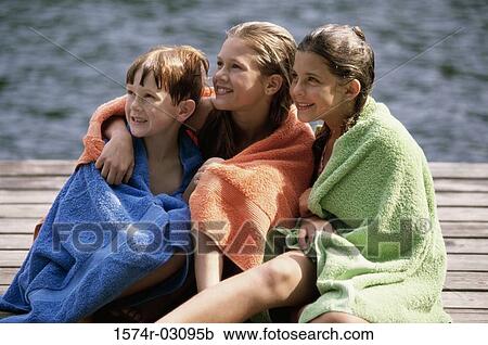 Two girls and a boy wrapped in towels sitting on a dock View Large Photo Image Stock Image - Two girls and a boy wrapped in towels sitting on a dock. Fotosearch