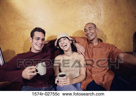 Stock Image - Two young men and a young woman sitting in a cafe drinking coffee. Fotosearch