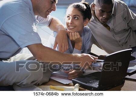 Stock Image - Two young men and a young woman using a laptop. Fotosearch