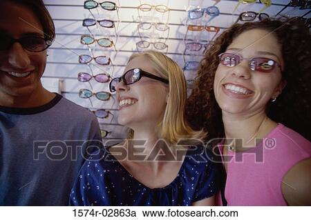 Stock Image - Two young women and a young man wearing sunglasses in a store. Fotosearch