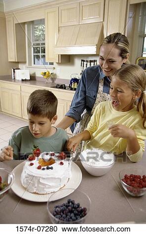 Stock Image - Woman icing a cake with her son and daughter. Fotosearch