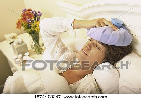 Stock Photo - Woman lying in bed holding a cold pack against her head. Fotosearch