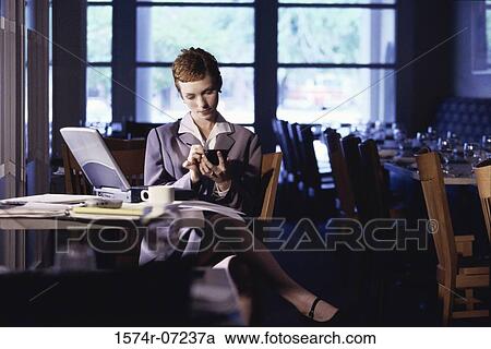 Stock Image - Woman sitting in a restaurant using a hand held device. Fotosearch