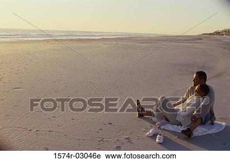 Stock Image - Young couple sitting on the beach. Fotosearch