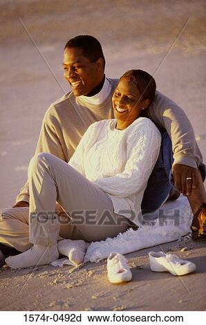 Stock Image - Young couple sitting together at the beach. Fotosearch