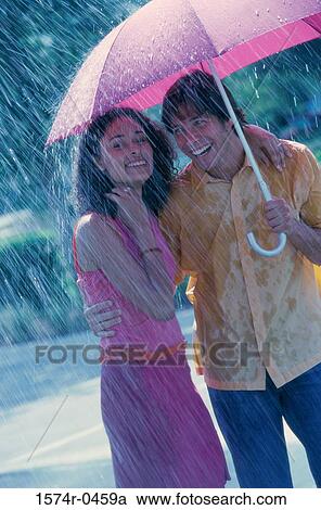 Stock Image - Young couple standing under an umbrella. Fotosearch
