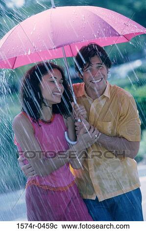 Stock Image - Young couple standing under an umbrella. Fotosearch