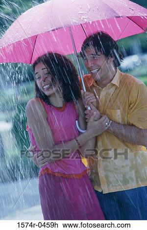 Stock Image - Young couple standing under an umbrella. Fotosearch
