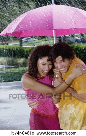 Stock Image - Young couple standing under an umbrella. Fotosearch