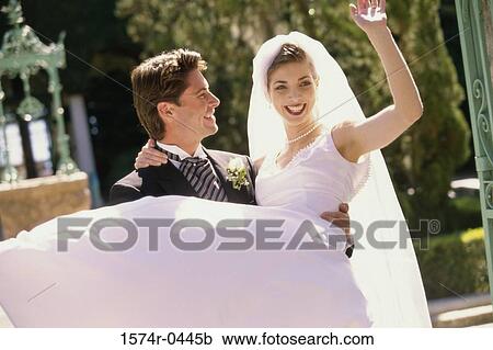 Stock Image - Young groom carrying his bride. Fotosearch