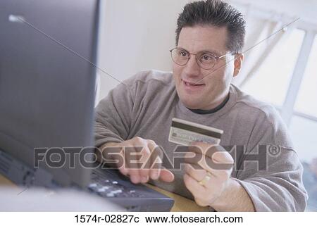 Young man sitting in front of a laptop holding a credit card View Large Photo Image Stock Image - Young man sitting in front of a laptop holding a credit card. Fotosearch