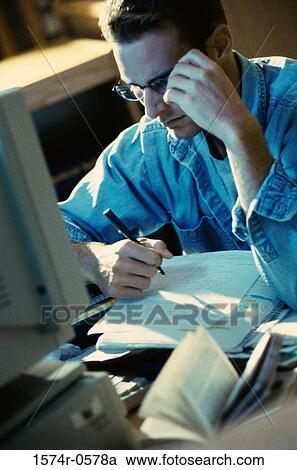 Young man sitting in front of a computer monitor writing View Large Photo Image Stock Image - Young man sitting in front of a computer monitor writing. Fotosearch