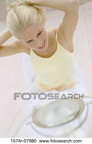 Stock Image - Young woman looking in a mirror adjusting her hair. Fotosearch