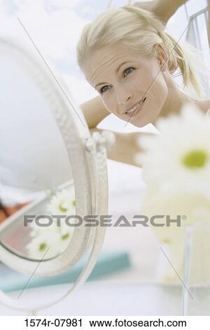 Young woman looking in a mirror adjusting her hair View Large Photo Image Stock Image - Young woman looking in a mirror adjusting her hair. Fotosearch