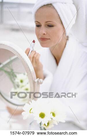 Stock Photo - Young woman sitting in front of a mirror applying make-up. Fotosearch