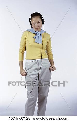 Stock Photo - Young woman standing and wearing headphones. Fotosearch