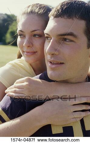 Stock Image - Young woman standing behind a young man with her arms around him. Fotosearch